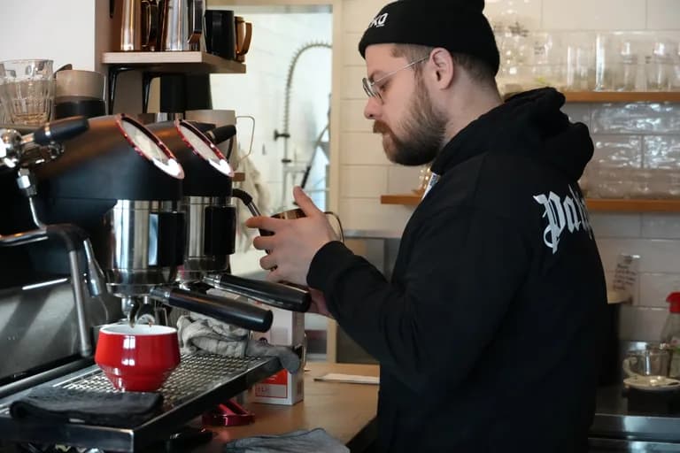 Barista schäumt Milch an der Espressomaschine im KOKO Coffee Lab Würzburg auf, rote Tasse auf der Theke